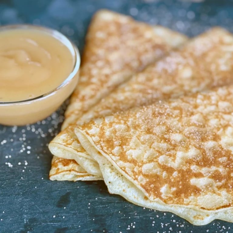 Cinnamon sugar coated pancakes stacked on a dark surface with a bowl of maple syrup alongside