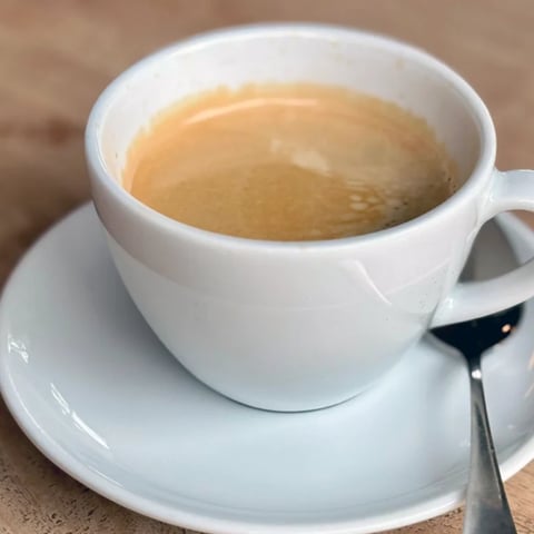 White ceramic cup filled with light brown coffee on a matching saucer with a spoon