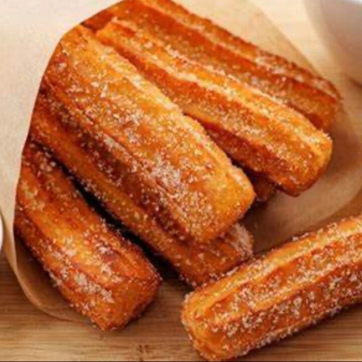 Four golden churros coated with cinnamon sugar on parchment paper and wooden surface