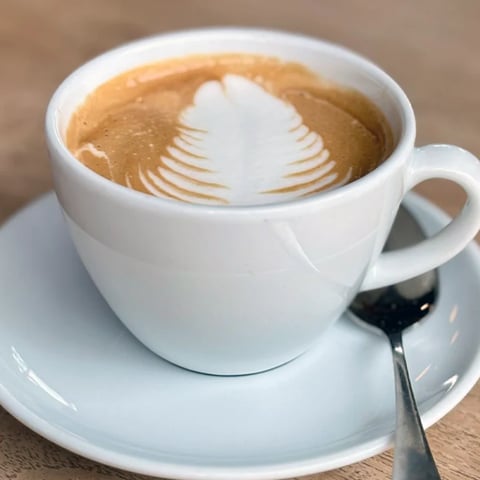 White coffee cup with latte art leaf design in foam on saucer with spoon