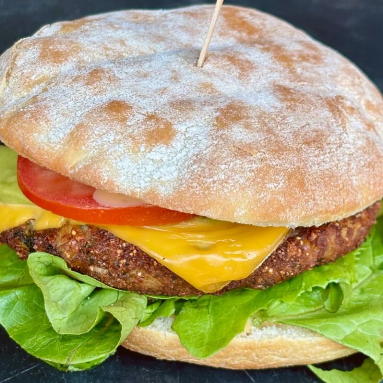 Gourmet cheeseburger with sesame seed bun, beef patty, melted cheddar cheese, tomato, and lettuce on dark background