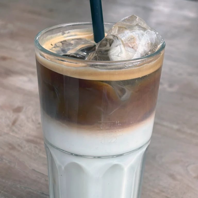 Iced coffee drink with layered milk and espresso in a clear glass with a blue straw on outdoor surface