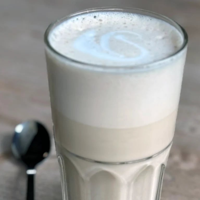 Glass of layered cappuccino or latte with white foam top and creamy layers, with a spoon visible in the foreground