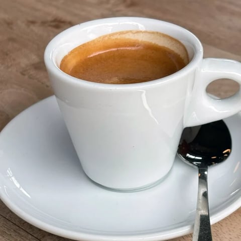 White coffee cup filled with espresso on a saucer with a small spoon, set on a wooden surface
